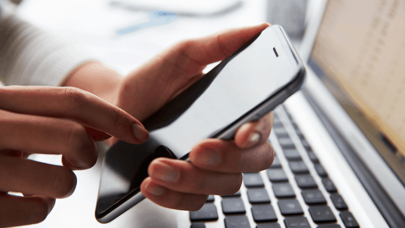 Person holding a smartphone over a laptop.