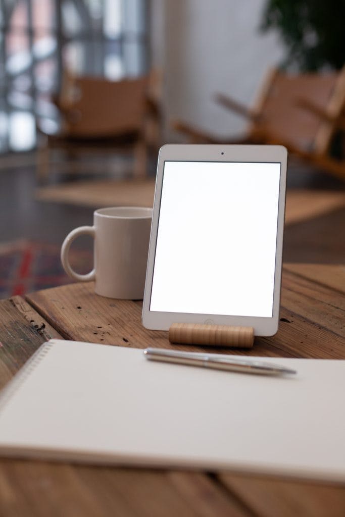 A tablet next to a pen paper and a mug