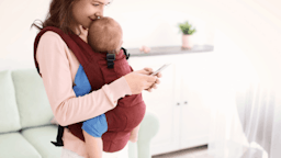 Mom holding baby in wrap looking down at phone.