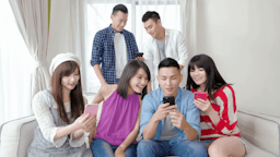 Group of 6 happy people on their smart phones in a living room